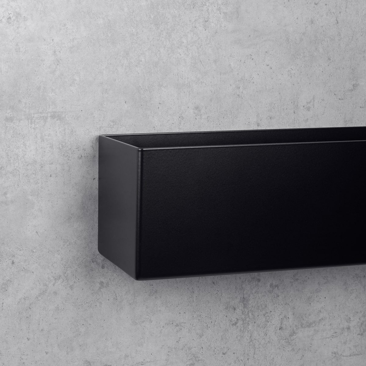 gros plan d'une étagère murale noire au design minimaliste, fixée à un mur gris texturé